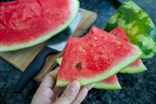 Hand holding slice of watermelon, with watermelons on the background. Selective focus