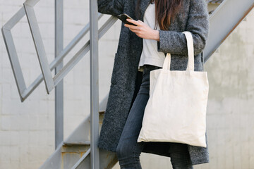 Woman holding white textile tote eco bag in urban area. Ecology or environment protection concept. White eco bag for mock up.