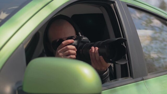 A man sitting in a car and taking a photo with a professional camera, a private detective or a paparazzi spy.