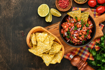 Traditional Mexican tomato sauce salsa with nachos and ingredients tomatoes, chile, garlic, onion on dark old wooden background. Concept of Latin American and Mexican food. Mock up.