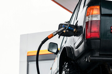 Off-road vehicle refueling with fuel nozzle at gas station in rainy day. Filling 4x4 car with...