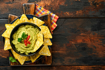 Guacamole. Traditional latinamerican Mexican dip sauce in a black bowl with avocado and ingredients and corn nachos. Avocado spread. Top view. Copyspace