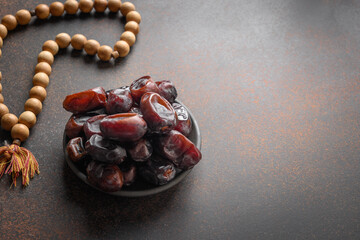 Ramadan. Wooden prayer beads and dates in bowl on brown. View from above. Eid Mubarak. Religious tradition.