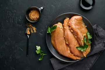 Raw chicken meat fillet marinated in teriyaki soy sauce, onions, garlic and pepper in black plate on a dark slate, stone or concrete background. Top view with copy space.