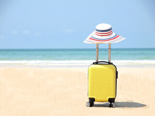 Fototapeta na wymiar Travel on Summer and tourist planning with yellow suitcase with white hat fashion in the beautiful beach. Travel in holiday. Blue sky and sand background, on travel in summer concept.
