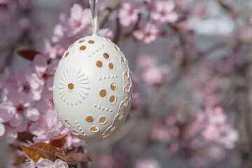 Decorative Easter egg hanging on flowering cherry tree with pink flowers. Easter background. Blossoms on a sunny spring day. Selective focus