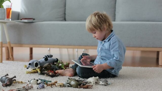 Cute blond child, toddler boy, playing at home with dinosaurs, sitting on the floor