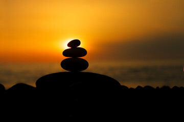 Rock pebble pyramid silhouette at sunset, zen stones on sea beach, meditation, spa, harmony, balance concept