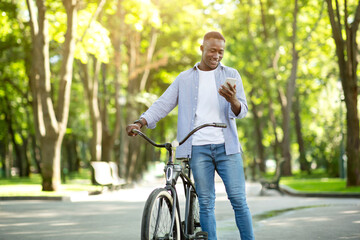 Obraz premium Funky African American guy with bicycle chatting on smartphone outdoors, space for text