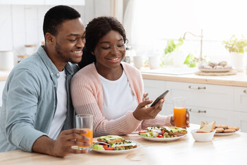 Obraz na płótnie Canvas Millennial Black Man And Woman Having Breakfast And Using Smartphone In Kitchen