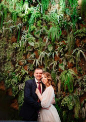 Obraz premium happy bride and groom at the wall decorated with live plants. 