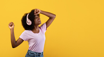 Music lover. African american lady enjoying music in wireless headphones on yellow background, panorama with empty space