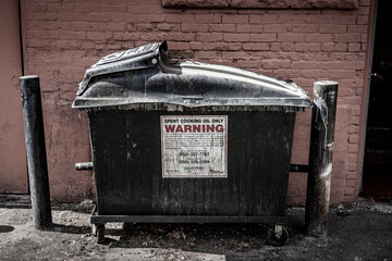 A dirty trash bin is a receptacle for used cooking oil outside a restaurant in a back alley .