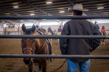 A horse stares through the iron gate as a cowboy watches riders in the arena of a rodeo in Boise, Idaho.