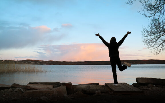Women raising hands in an amazing landscape during a pink sunset. Calm lake in the background (Scandinavia, Sweden).