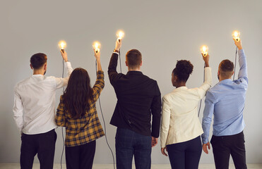 Group of young multiethnic business professionals holding up shining Edison light bulbs standing on...