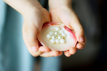 Children's hands hold oyster shell with pearls	