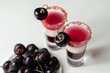 Three-layer cocktail based on vodka, cherry liqueur and syrup in drink shot glass, decorated with fresh cherry and red sugar