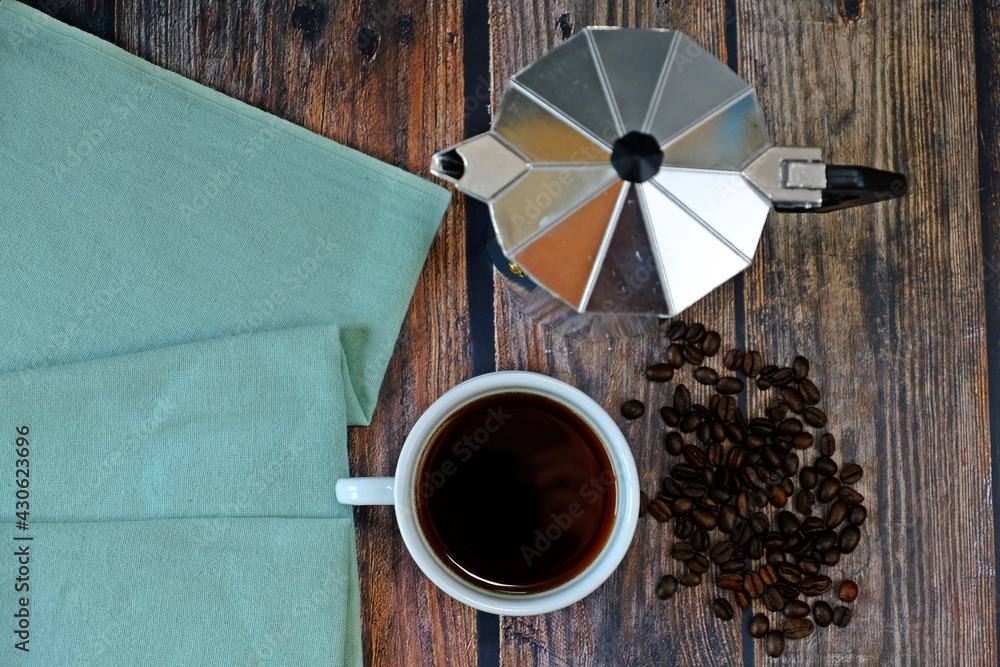 Wall mural a cup of hot black coffee with moka pot and coffee beans on wooden table.