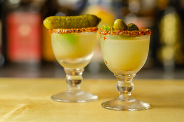 Shaken vodka and pickle juice with ice in shot glass and garnishing with small pickled cucumber and...