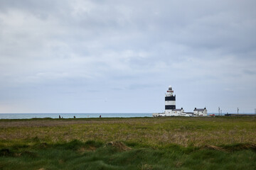 Fototapeta na wymiar panorama of hook lighthouse and green meadow with cloudy sky. Wexford, Ireland.