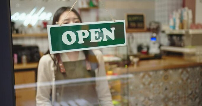 Sad female coffee shop owner shutting down business deu to pandemic, virus. Young Asian woman in medical mask putting up announcement Sorry, We're Closed and flipping OPEN sign. Covid-19 quarantine.