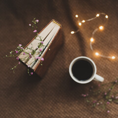 A book with flowers and cup of coffee on dark background top view