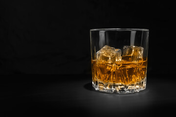 Close up of a glass with an alcoholic drink with ice on a black background.