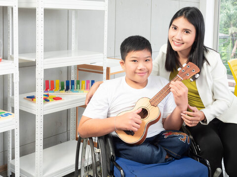Portrait of a beautiful Asian teacher and a disabled child in a wheelchair is playing the ukulele in a special classroom. Concept disabled child learning in school.