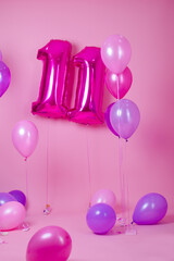 colorful blue, pink and purple balloons near air balloons shaped number eleven . on pink background. concept of birthday party celebration