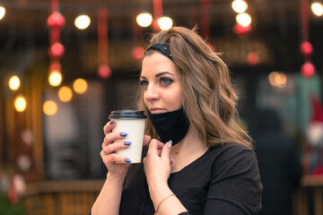 A sweet female of caucasian appearance in a black face mask, sits and works in an Internet cafe.