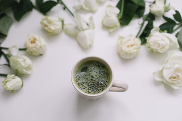 A cup of green matcha tea with white roses on white background view from above. Flatlay, top view, copy space