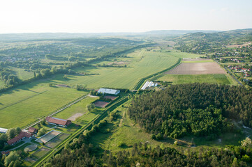 A view from a hot air balloon to fields, trees and one-story houses on the ground.