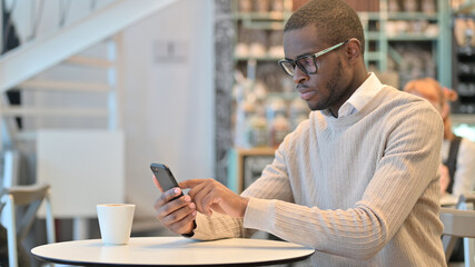 Fototapeta na wymiar Attractive African Man using Smartphone in Cafe 