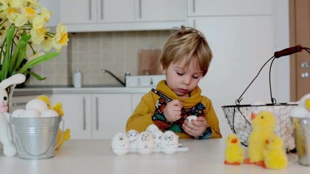 Toddler child, boy, drawing funny emoticons on easter eggs with black pen