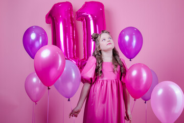 sweet brunette girl with pink make up and in pink leather dress. near colorful balloons in shape of number eleven. on pink background.concept of joy, party, birthday celebration.
