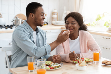 Romantic Black Man Feeding His Wife With Toast During Breakfast In Kitchen