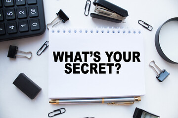 Notepad with text WHAT'S YOUR SECRET on the office desk with stationery. A blank notepad for entering a copy or text. business