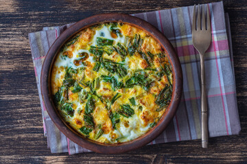 Ceramic bowl with vegetable frittata, simple vegetarian food. Frittata with egg, pepper, onion, cheese and green wild garlic leaves on table