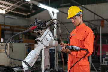Male engineer checking robotic arm machine for system welding with remote control at a factory Industrial