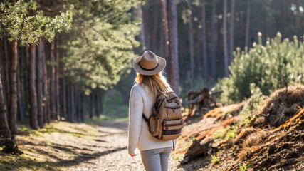 Woman with hat and backpack hiking in woodland.  Adventure in nature. Female tourist walking in...