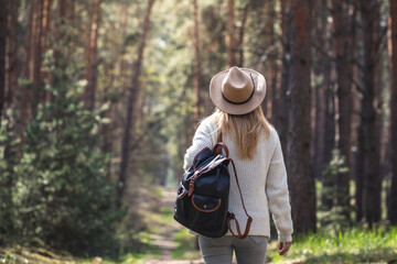 Woman with hat and backpack hiking in woodland.  Adventure in nature. Female tourist walking in forest alone