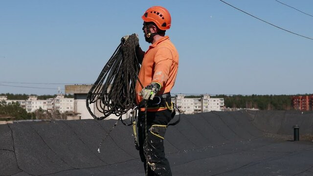 Tired and dirty industrial climber with beard pulling the rope on the roof after work. Sunset. Outside