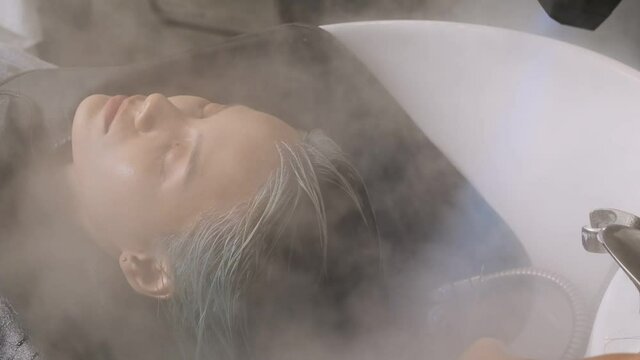 Female hairdresser uses steaming blue steam dryer for her clients' hair treatments,slow motion shot.