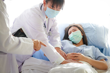 Two Asian doctors examined the abdominal pain of a woman lying in a hospital bed. Treatment of...