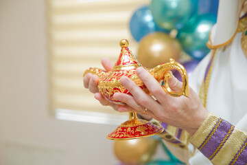 A man in Aladdin's clothes . A person holds in his hand realistic golden lamp of Aladdin . olds in...