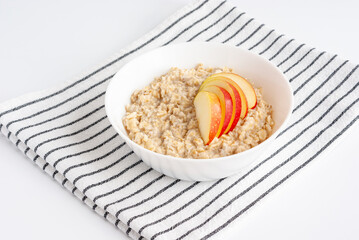 Oatmeal porridge with apples in white bowl on striped napkin. Vegan breakfast.