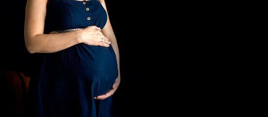 pregnant woman in a blue dress on a dark isolated background banner, space for text, selective focus