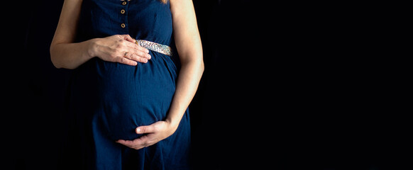 pregnant woman in a blue dress on a dark isolated background banner, space for text, selective focus
