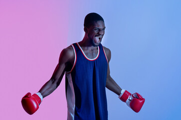 Aggressive black sportsman in boxing gloves shouting in anger in neon light. Combat sports concept